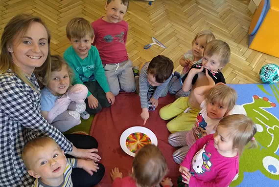 Opiekunka i grupa dzieci siedzące na dywanie podczas wspólnej zabawy w żłobku
